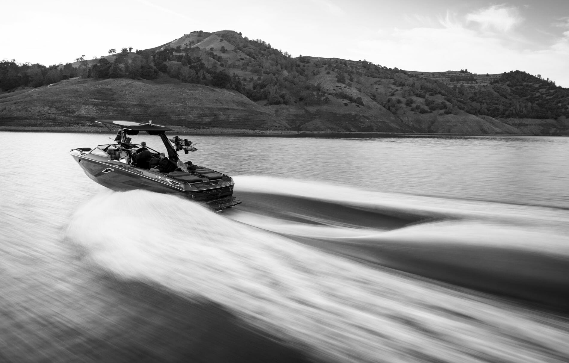 A black and white photo of a wakesurf boat on the water.