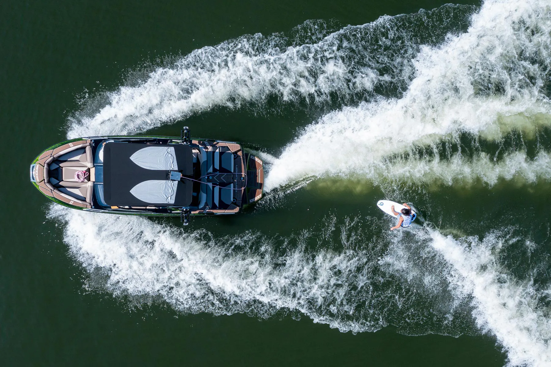 An aerial view of a person riding a wakesurf board on a boat.