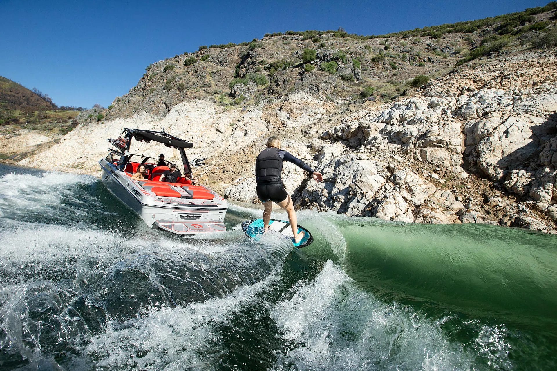 A man on a wakesurf board riding a wave behind a wakeboat.