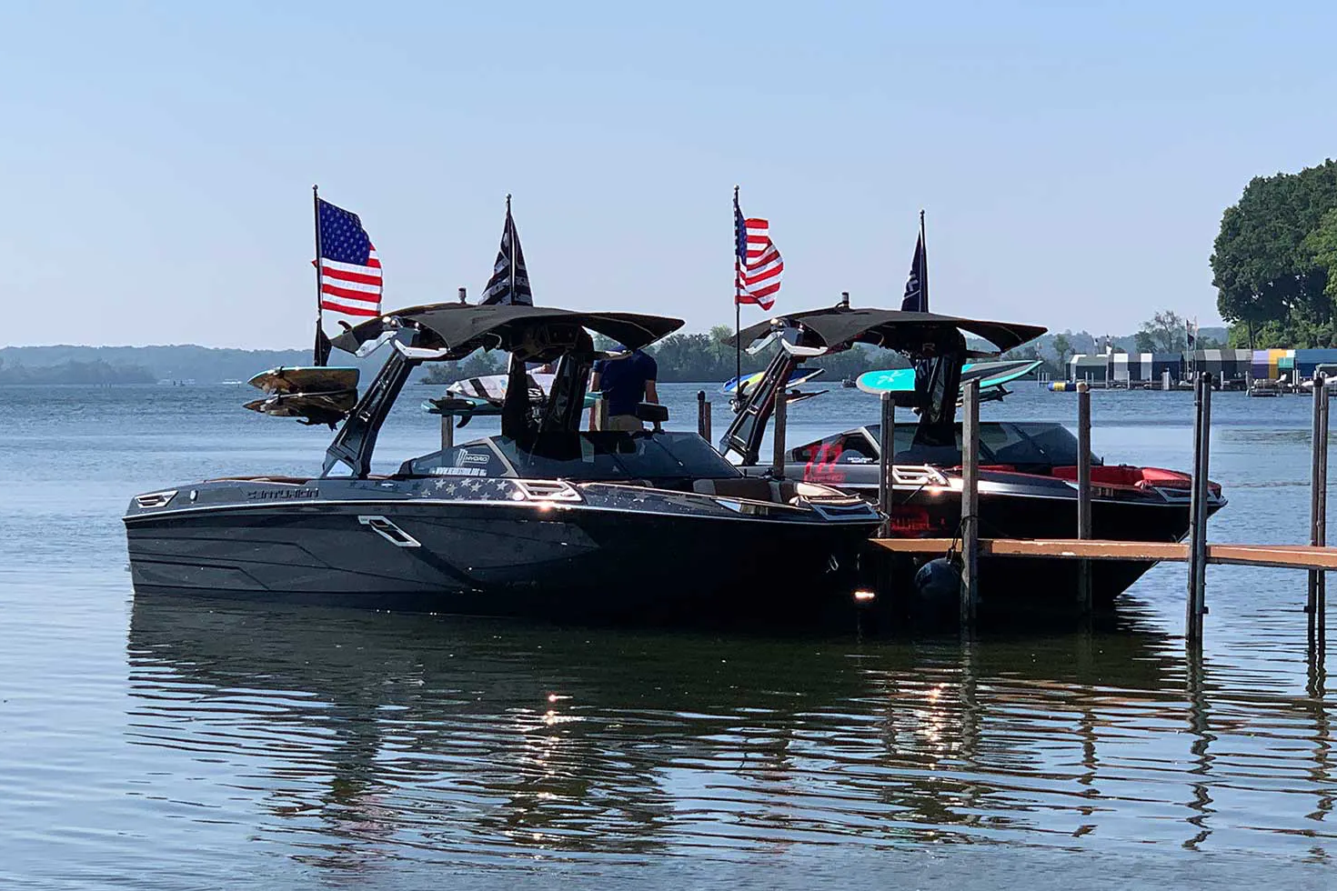 Two wakesurf boats docked at a dock with American flags.