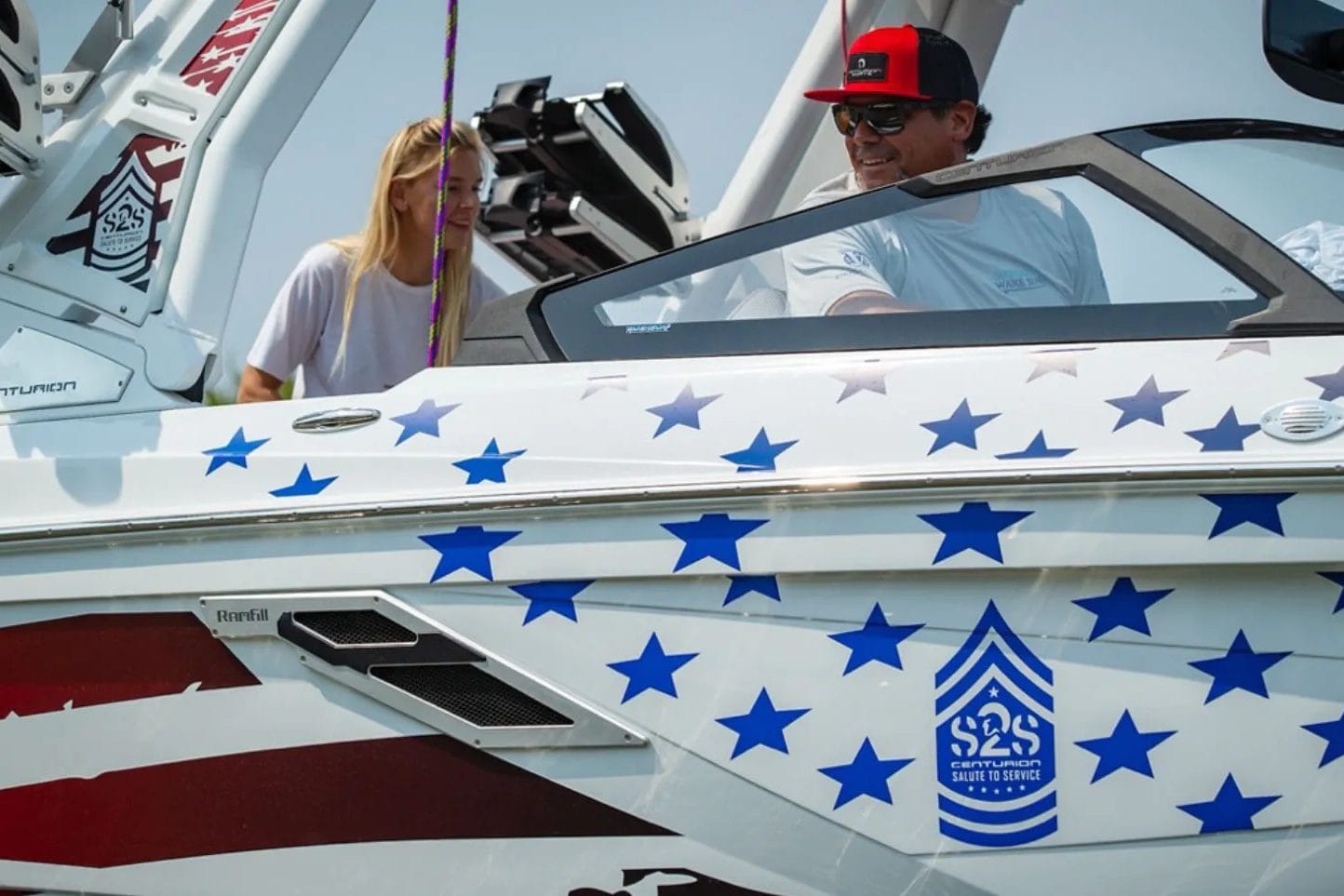 A man and woman on a wakesurf boat with an American flag on it.