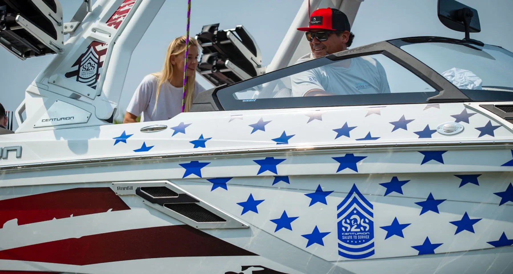 A man and woman on a wakesurf boat with an American flag on it.
