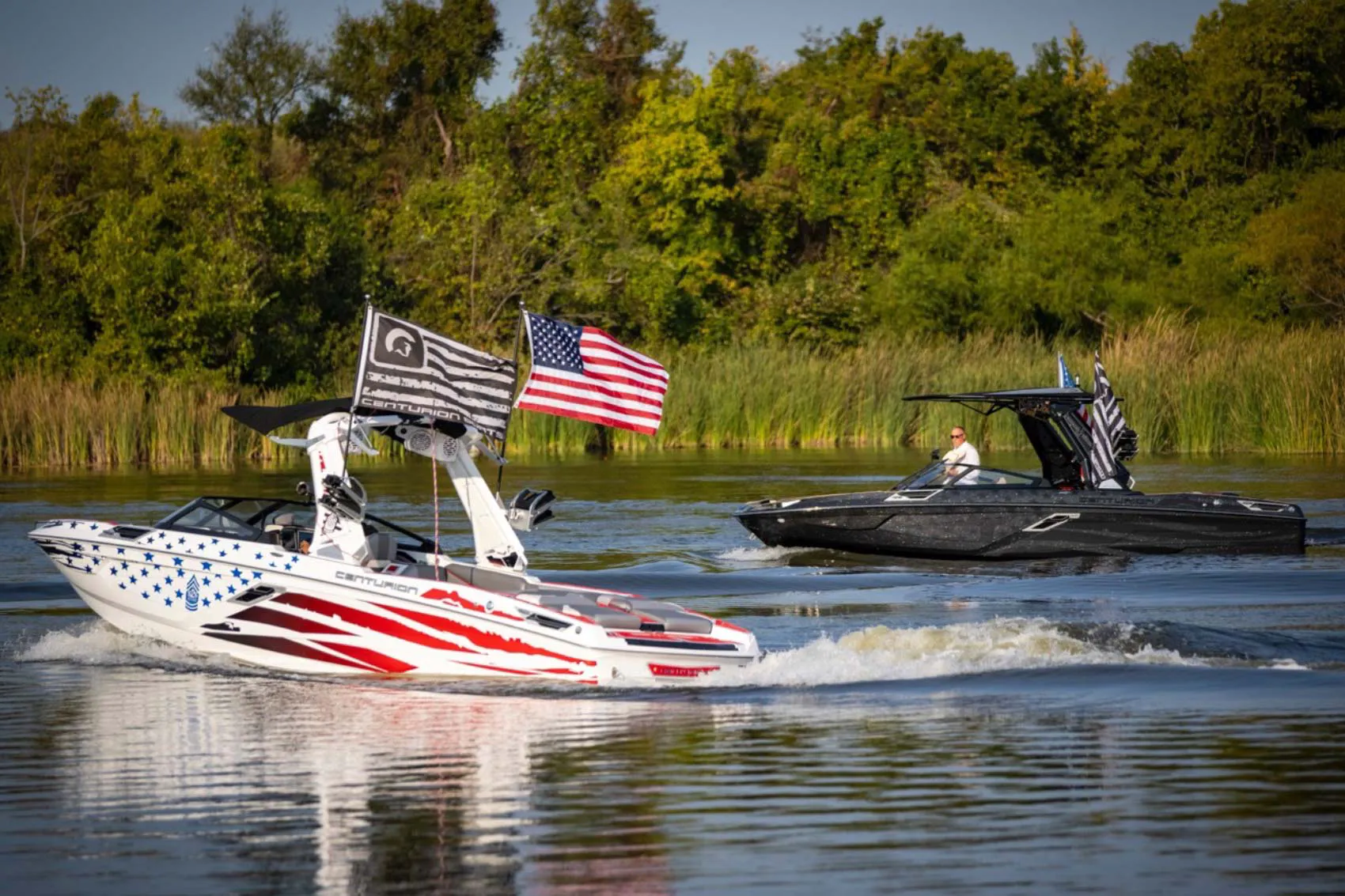 Two wakeboats with American flags on the water.