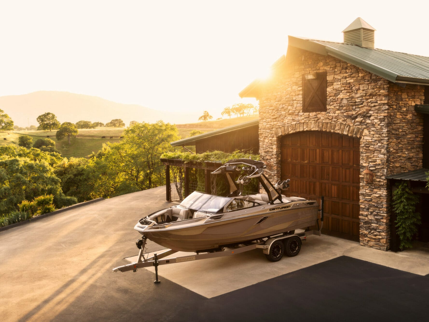 A wakesurf boat is parked in front of a barn.