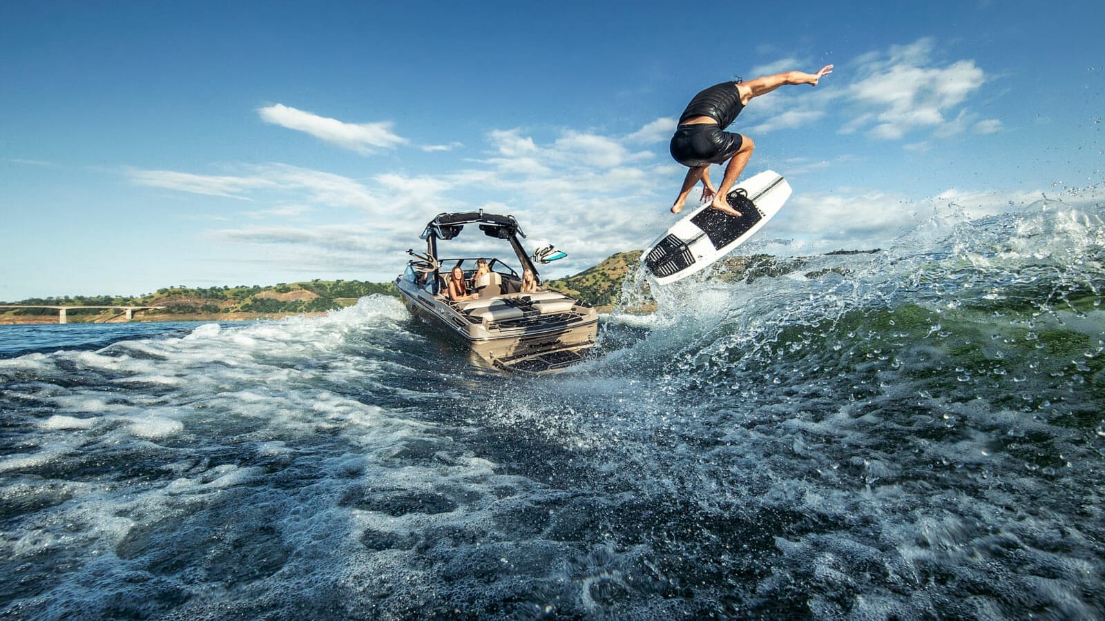 A man on a wakesurf board jumping off a boat.