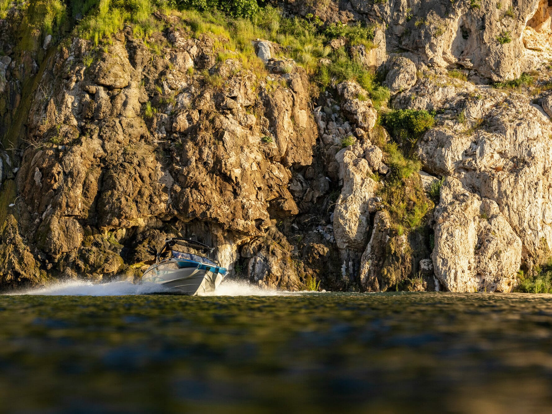 A wakesurf boat cruising near a cliff.