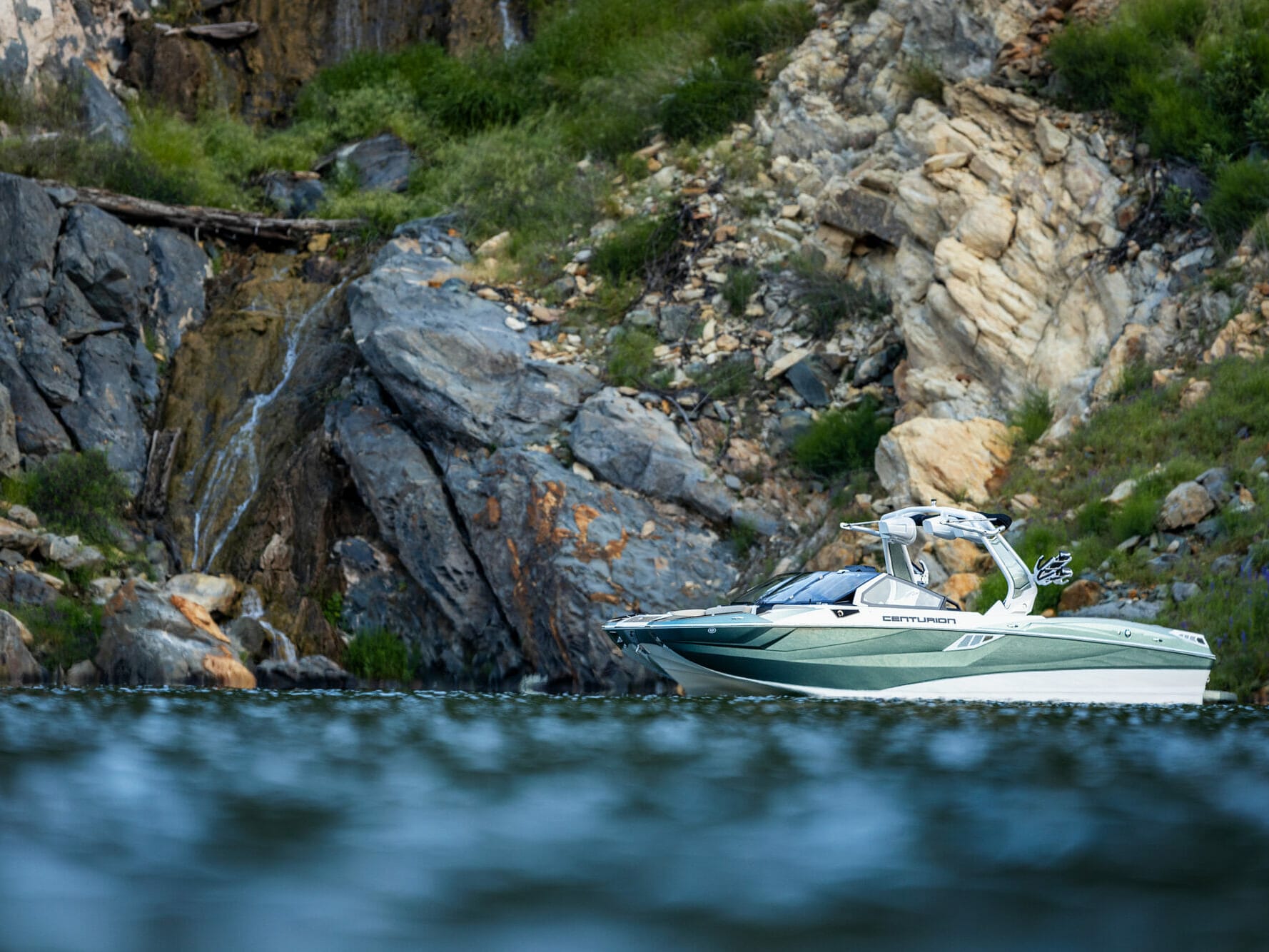 A wakesurf boat on the water near a rocky cliff.