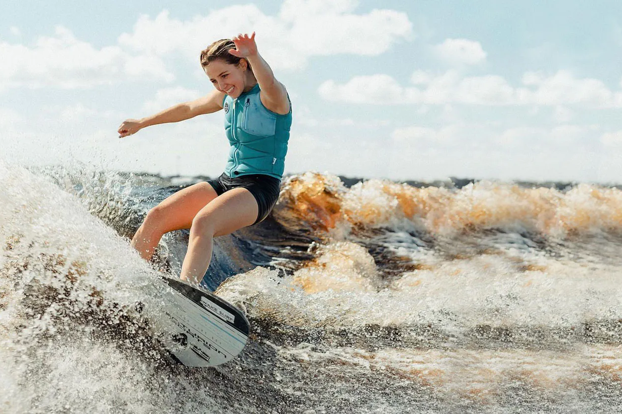A woman riding a wave on a wakesurf board.