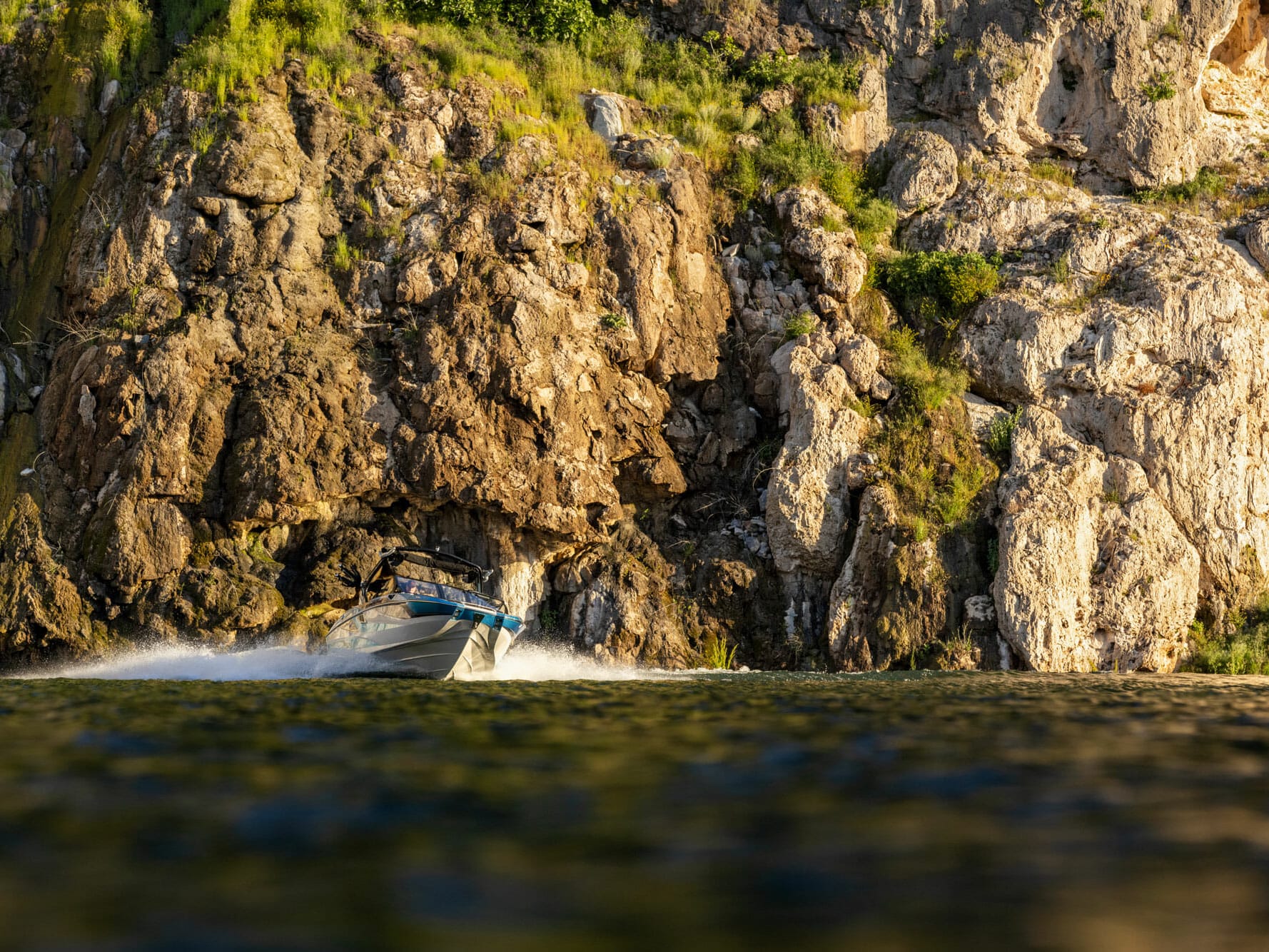 A wakeboat speeding near a cliff.