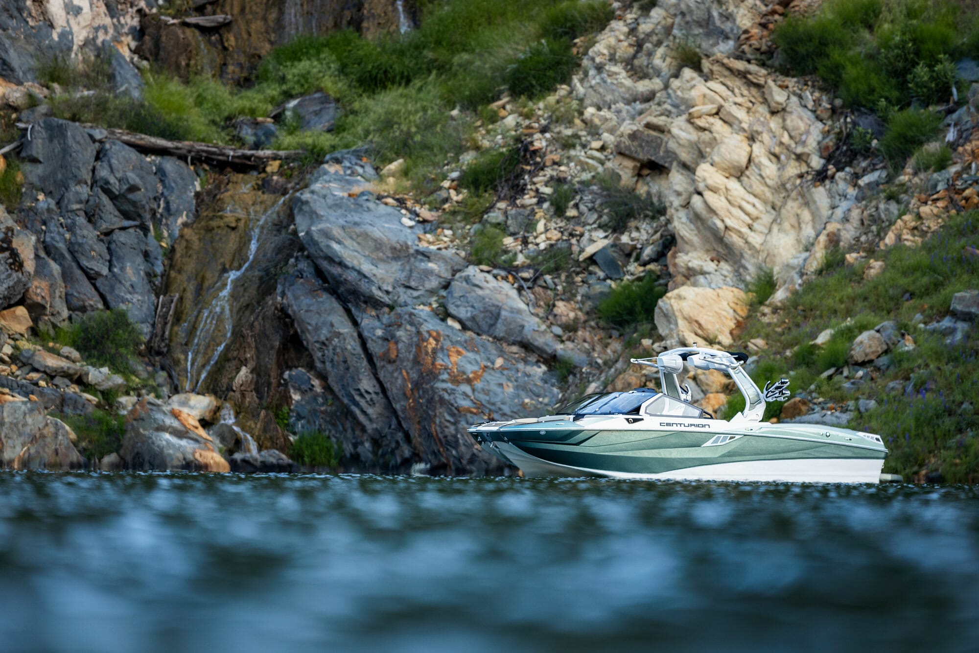 A wakesurf boat near a rocky cliff.