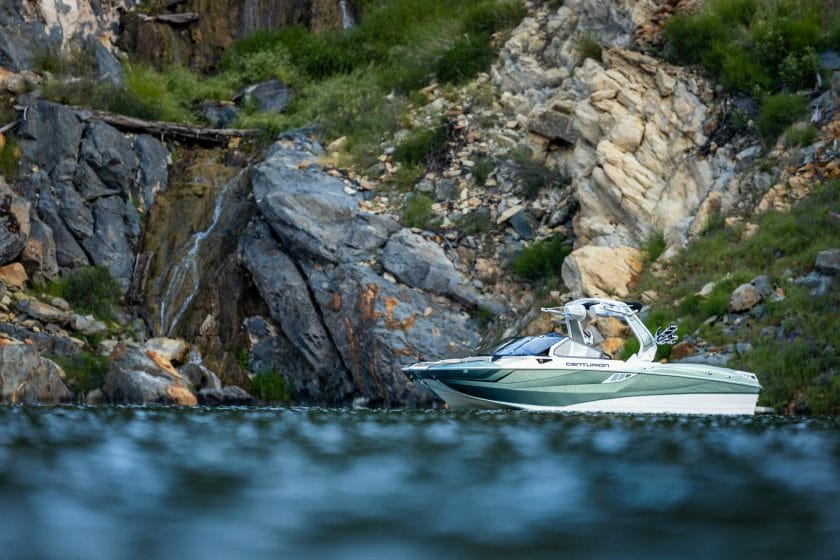 A wakesurf boat near a rocky cliff.