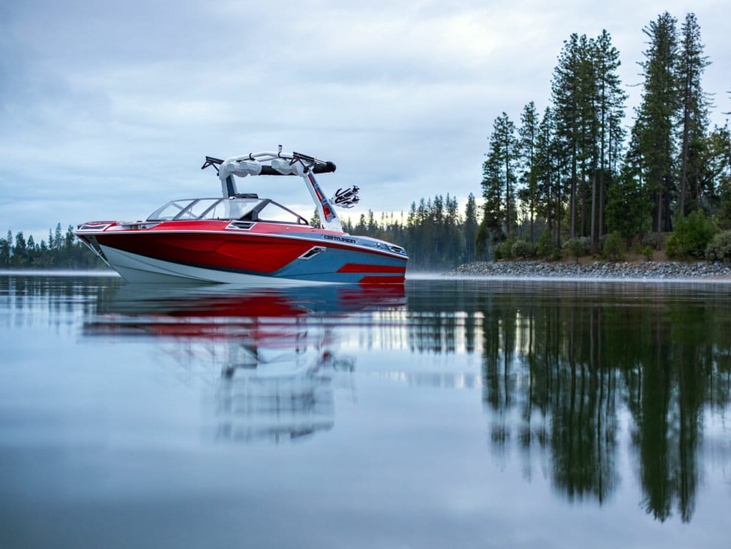 A red and white wakesurf boat on a calm body of water.