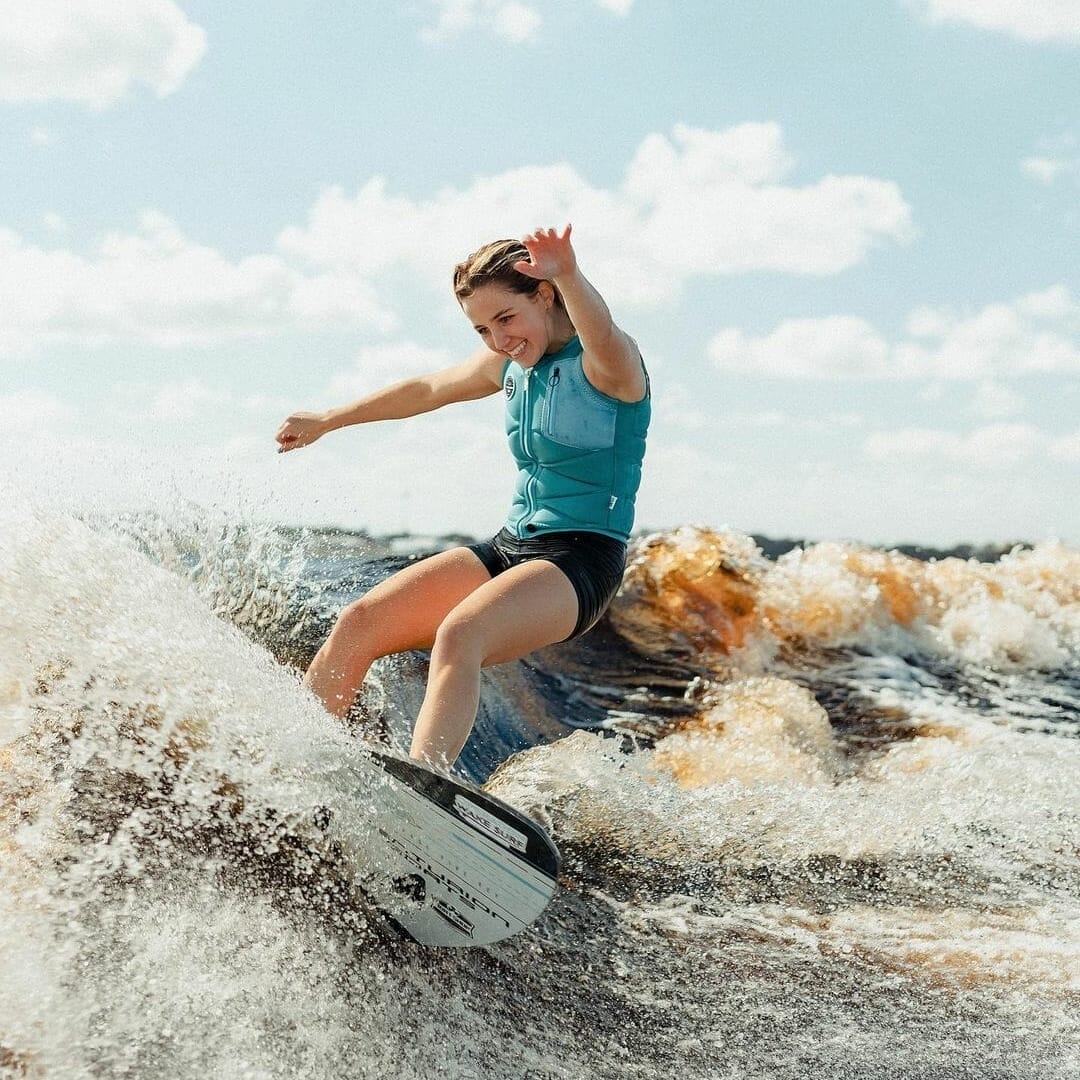 A young woman surfing a wave on a wakesurf board.