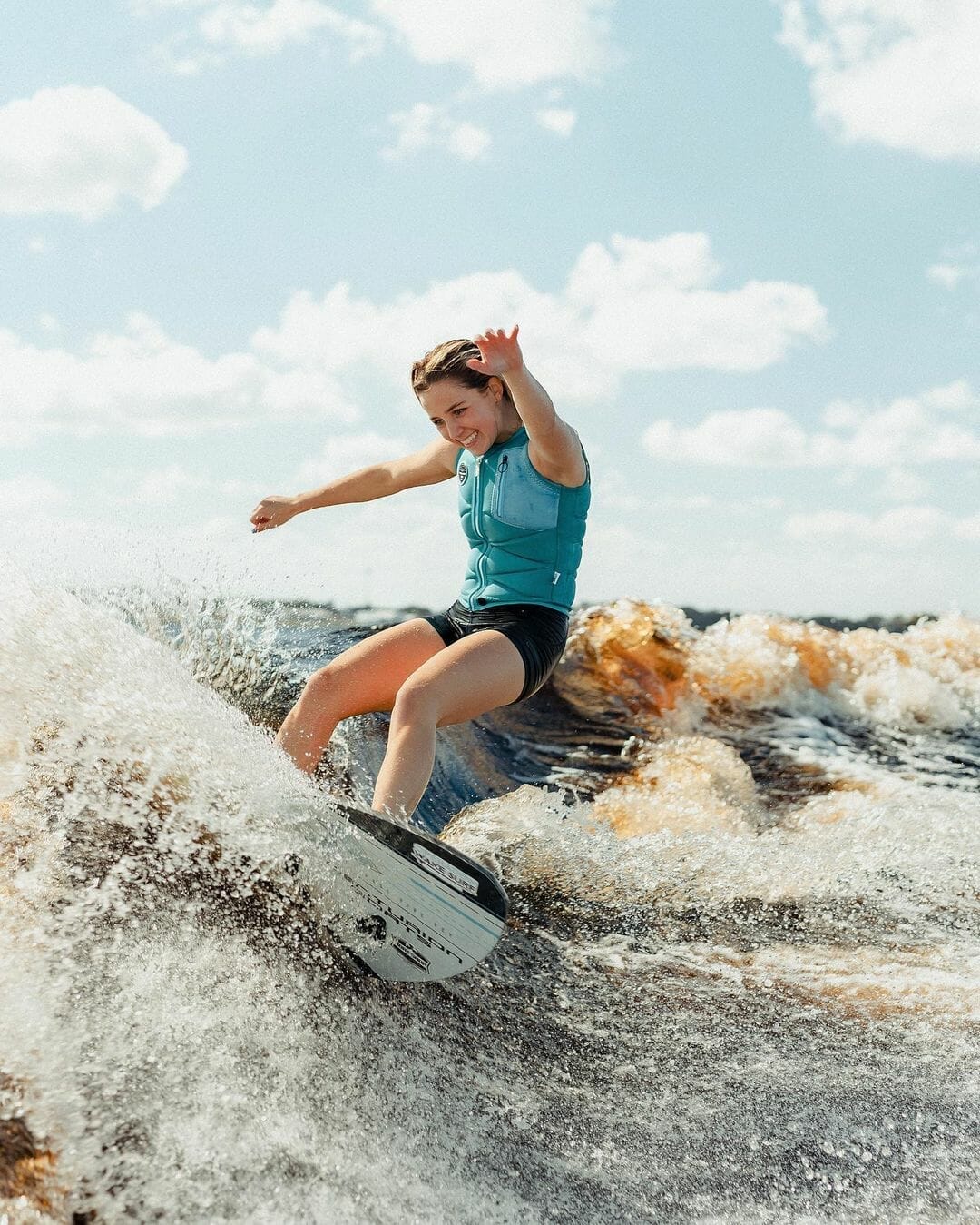 A young woman surfing a wave on a wakesurf board.
