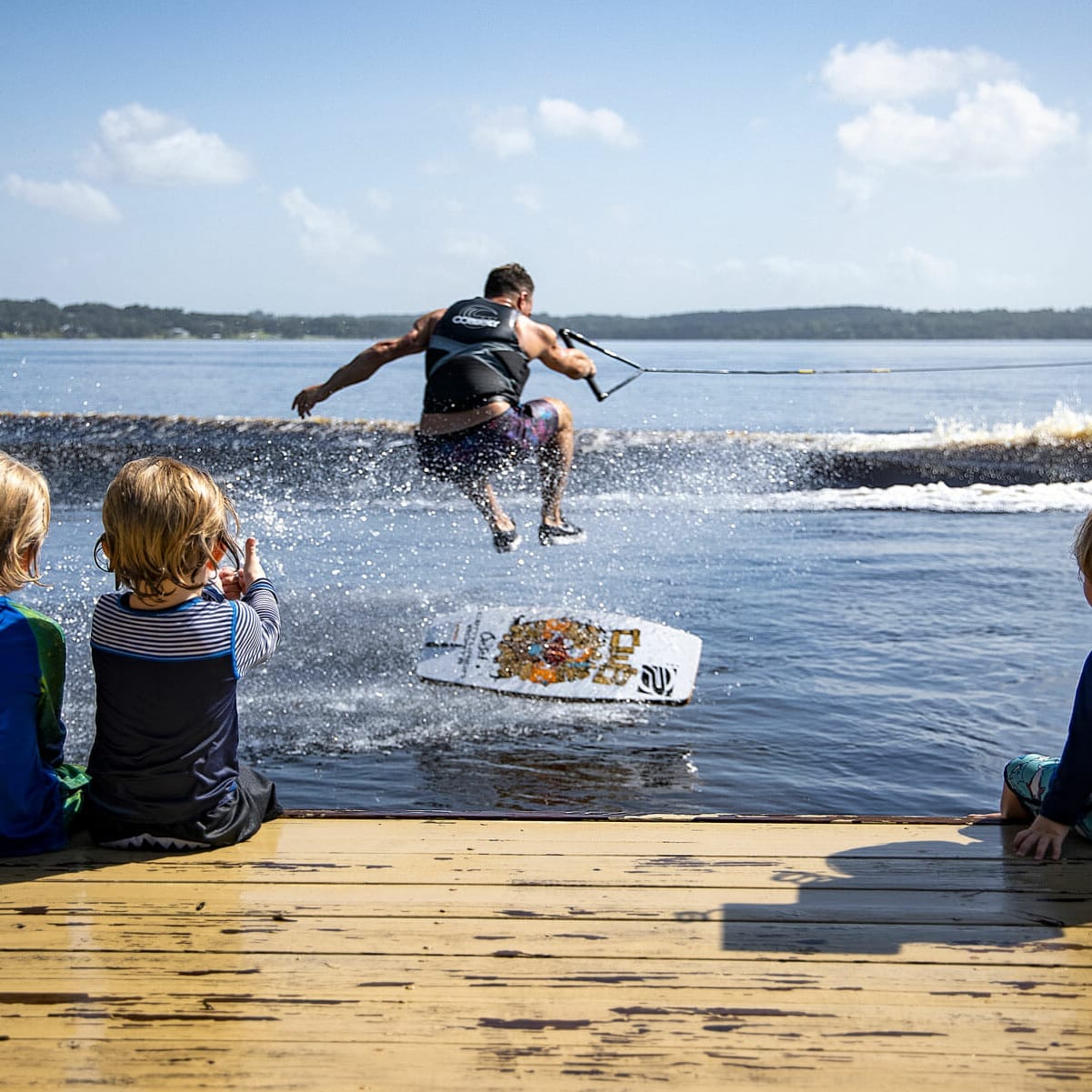 A group of children watching a man on a wakesurf board.