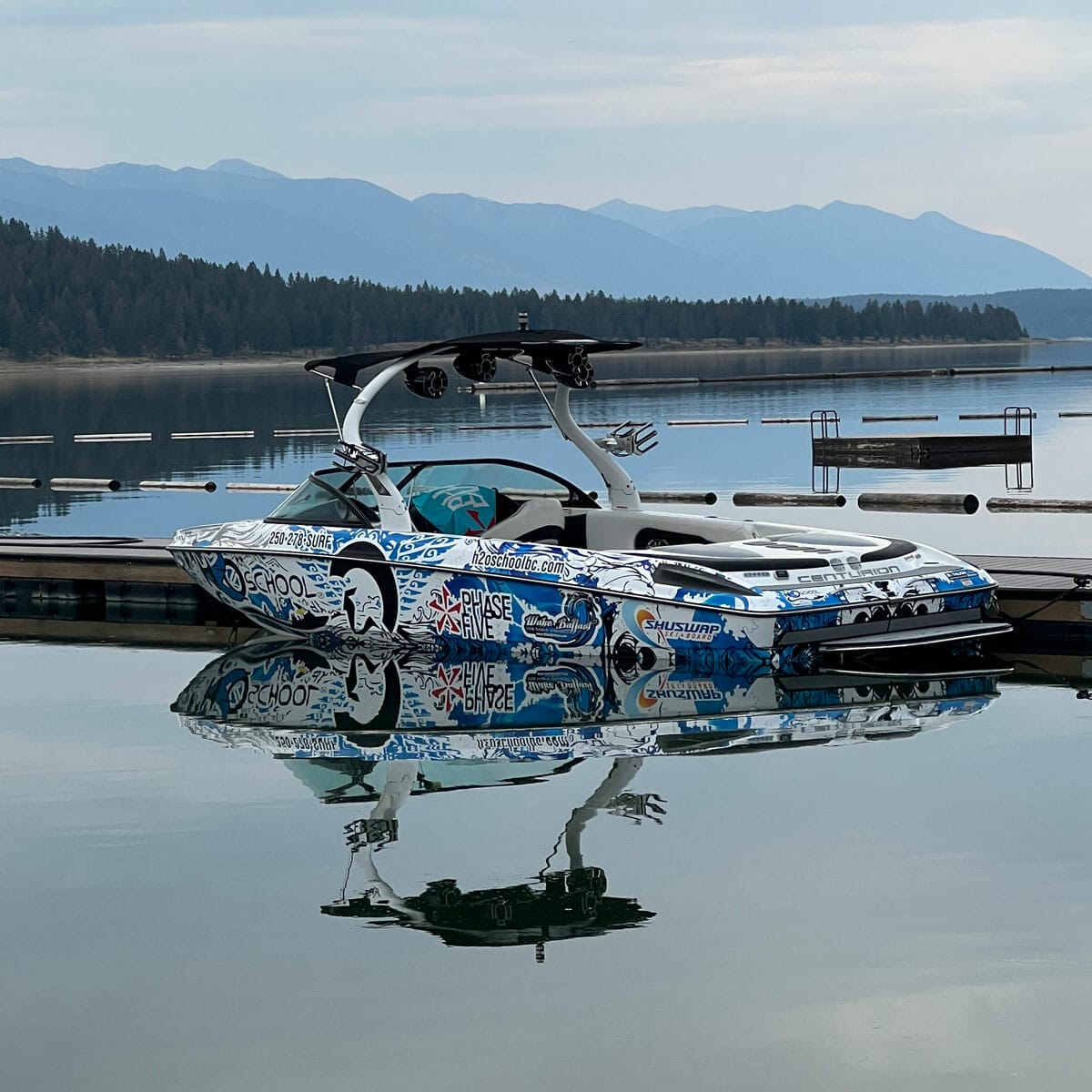 A wakeboat docked in a lake with mountains in the background.