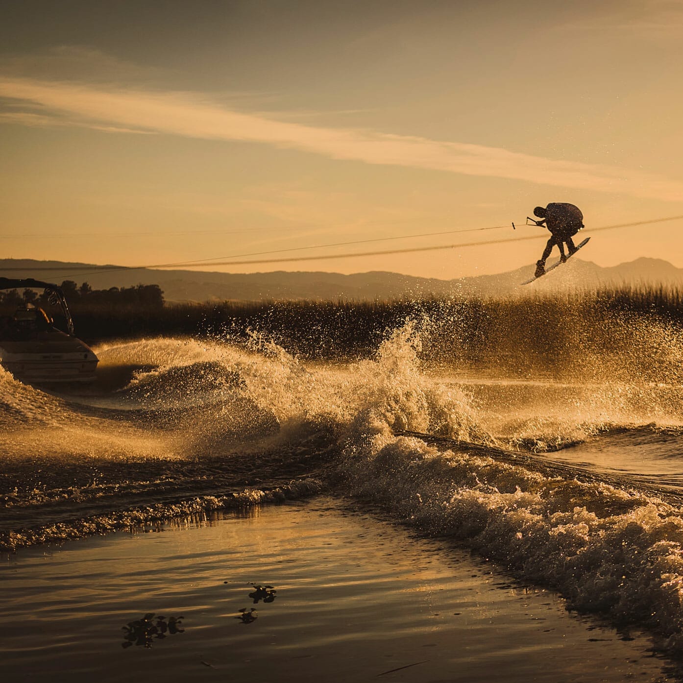 A wakesurfer jumps off a wakesurf boat at sunset.