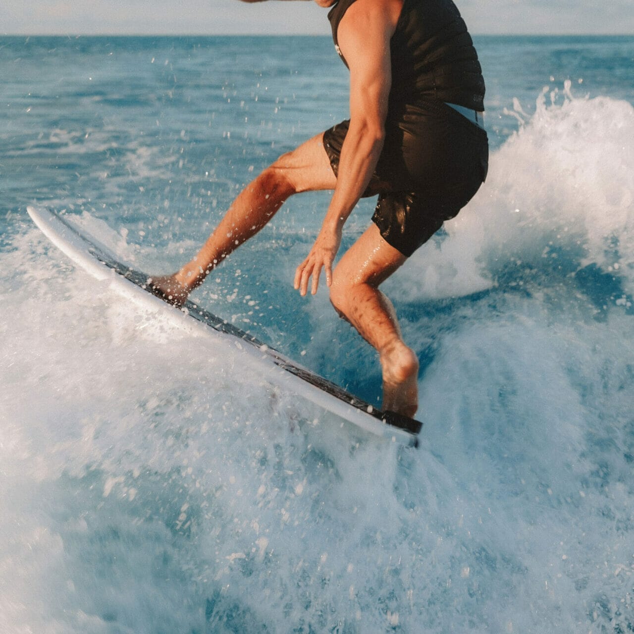 A man riding a wave on a surfboard behind a wakesurf boat.