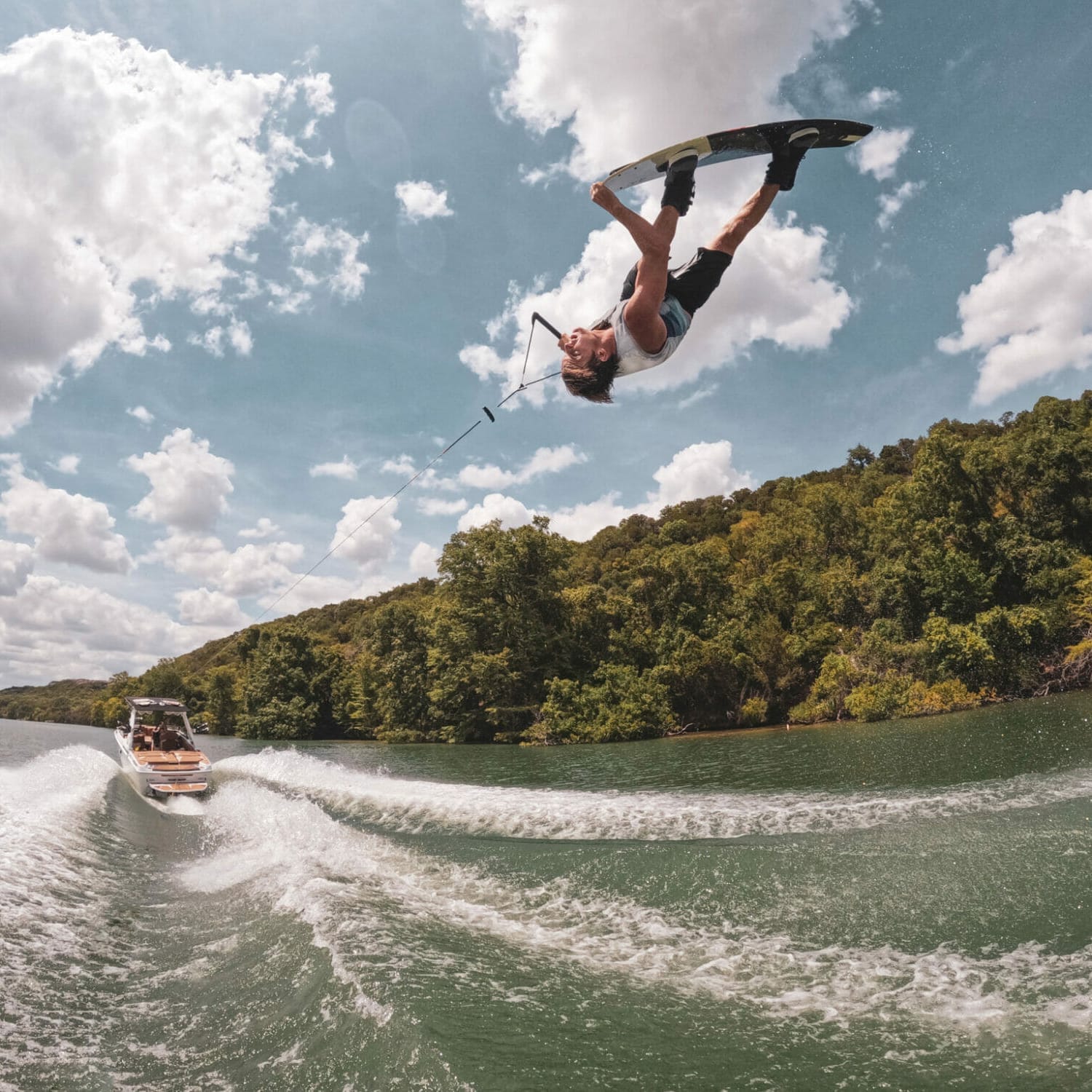 A man wakesurfing with a wakeboat in the background.