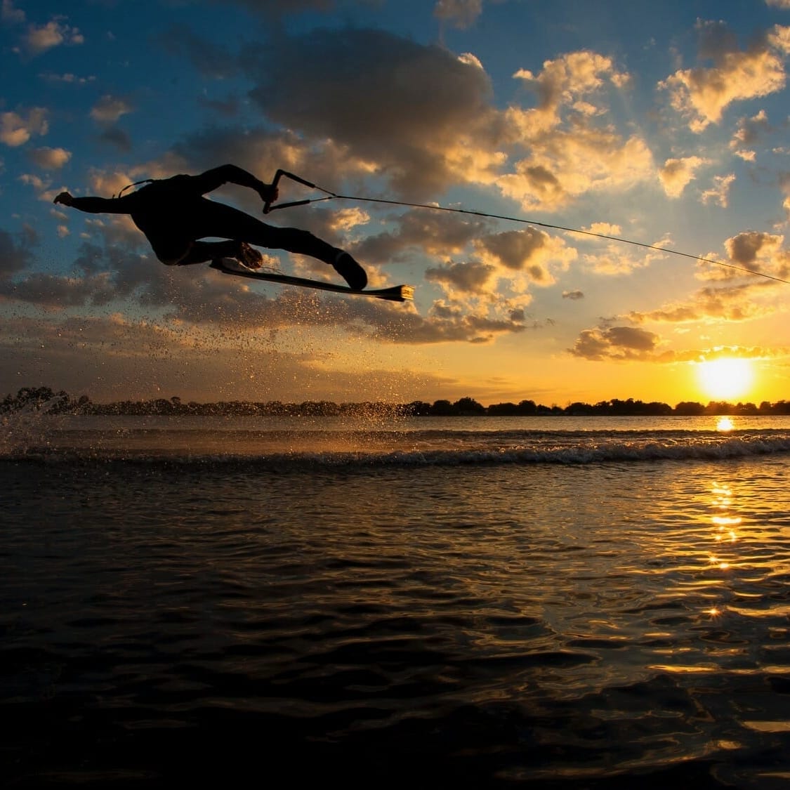A person wakeboarding on a wakesurf board at sunset.