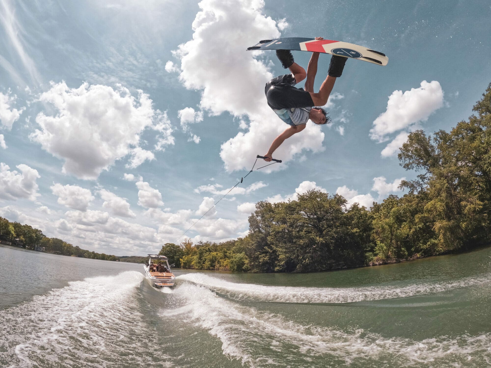 A man performing a trick on a wakeboard behind a wakeboat.
