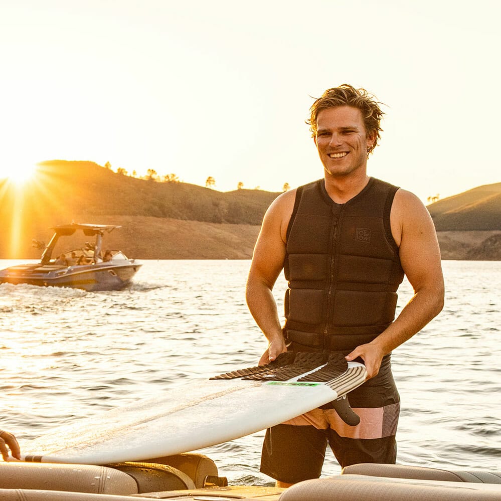 Two men on a wakesurf boat holding surfboards.
