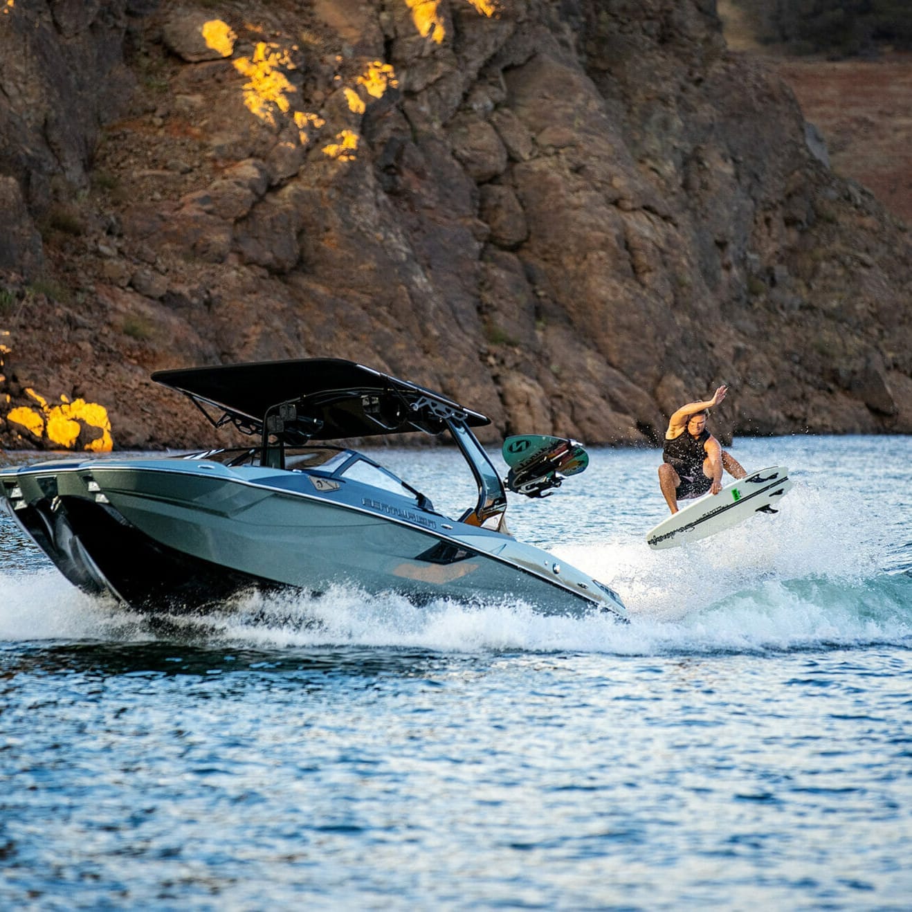 A person is riding a wakesurf board on a wakeboat.
