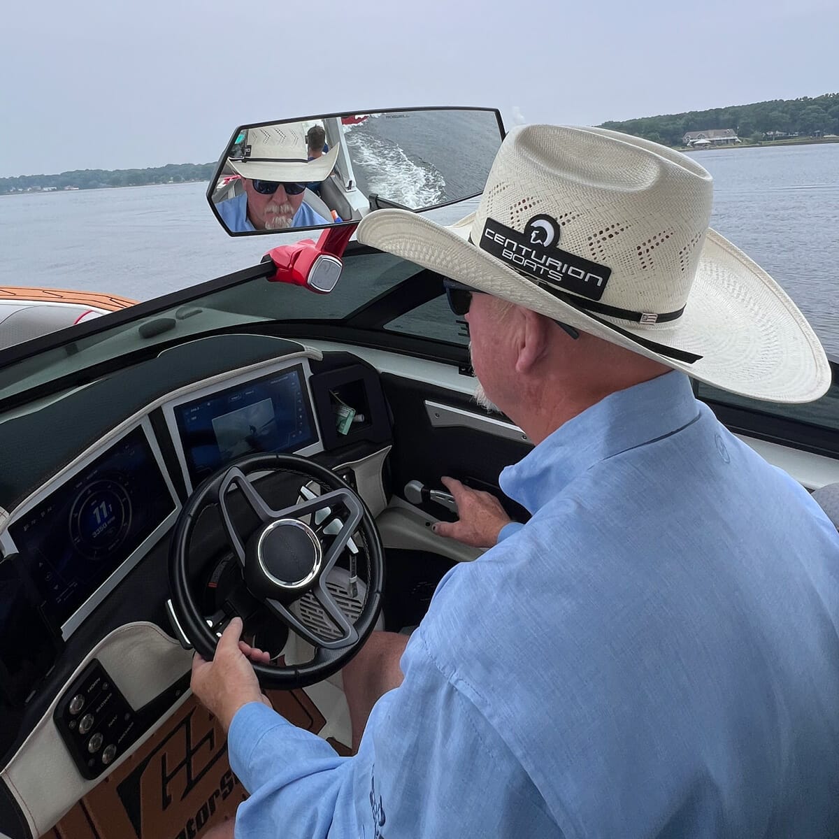 A man in a cowboy hat is driving a wakesurf boat.