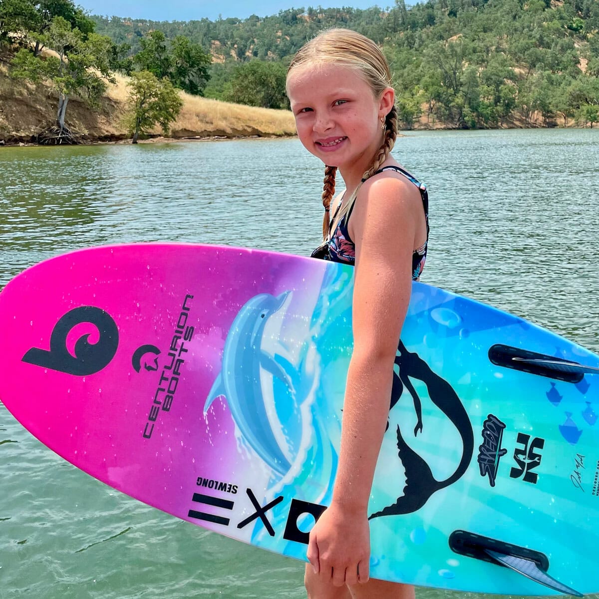 A young girl holding a wakesurf board in the water.