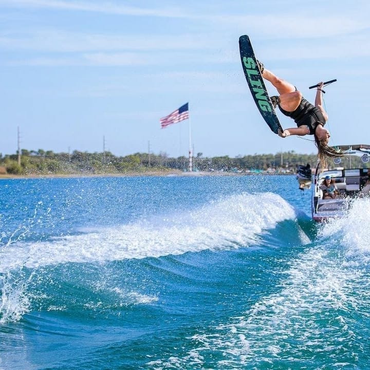 A person performing a wakeboard stunt behind a wakesurf boat.