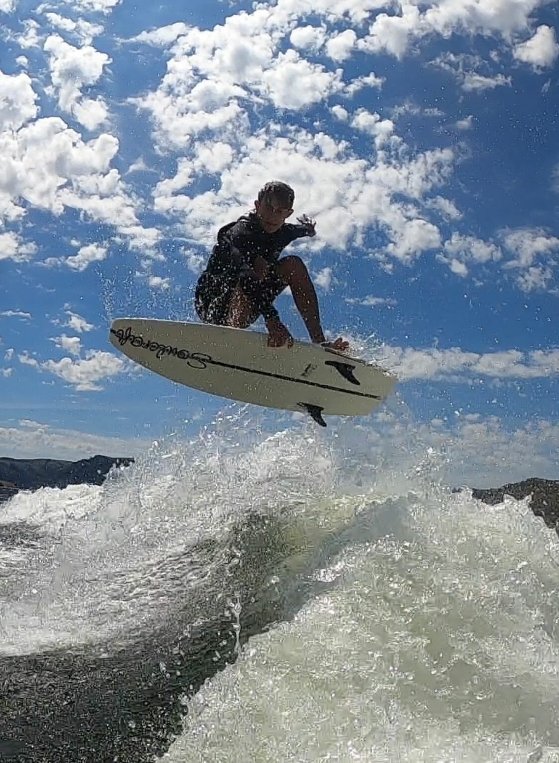 A man riding a wakesurf board in the air behind a wakeboat.