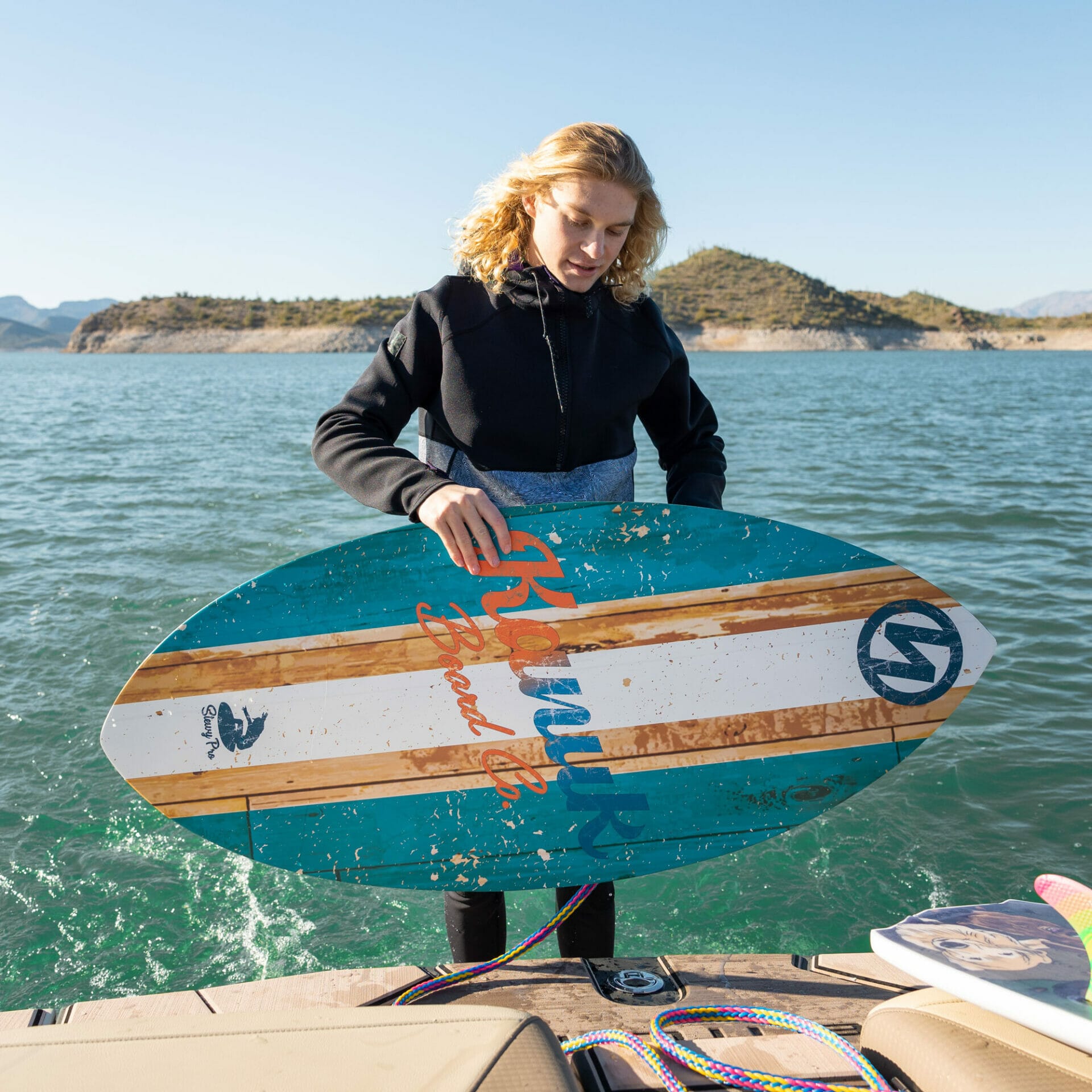 A woman holding a wakesurf board on a boat.