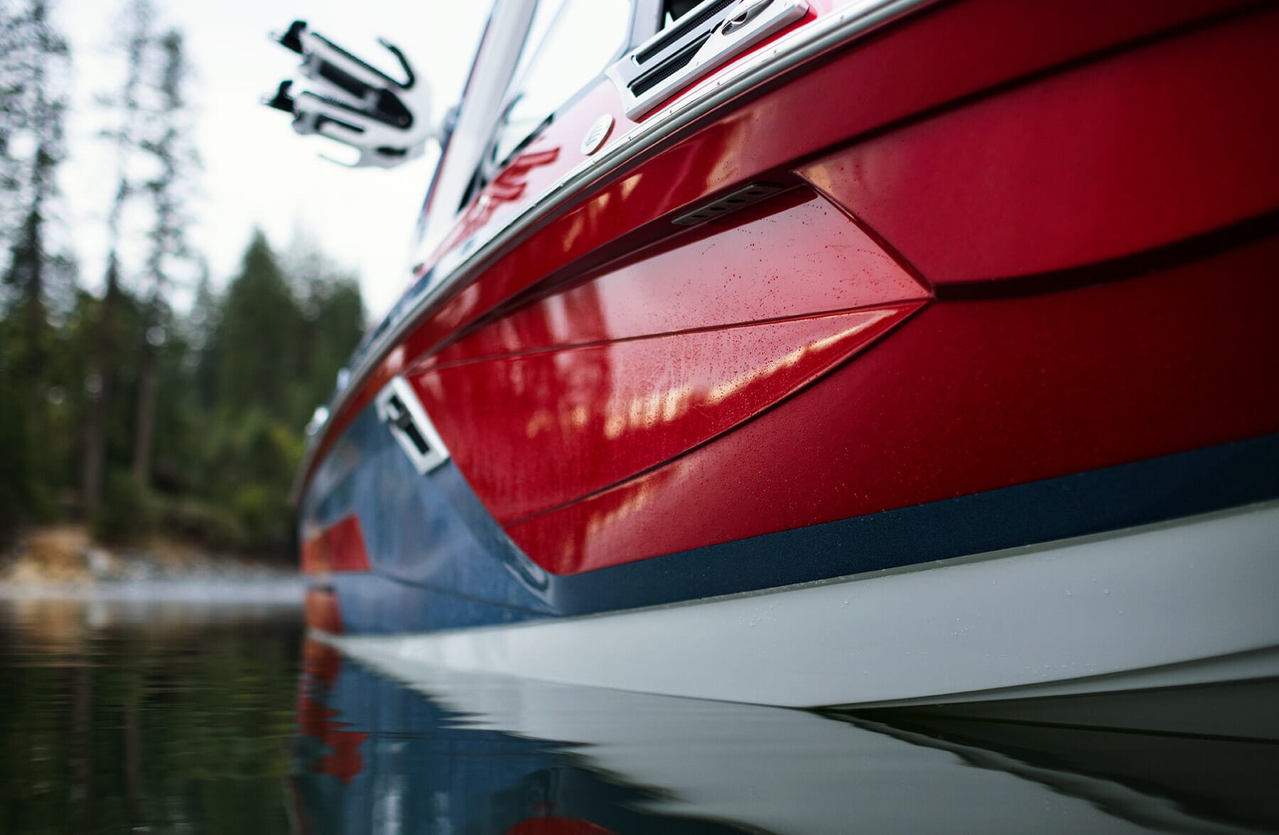 A red and blue wakesurf boat is sitting on the water.