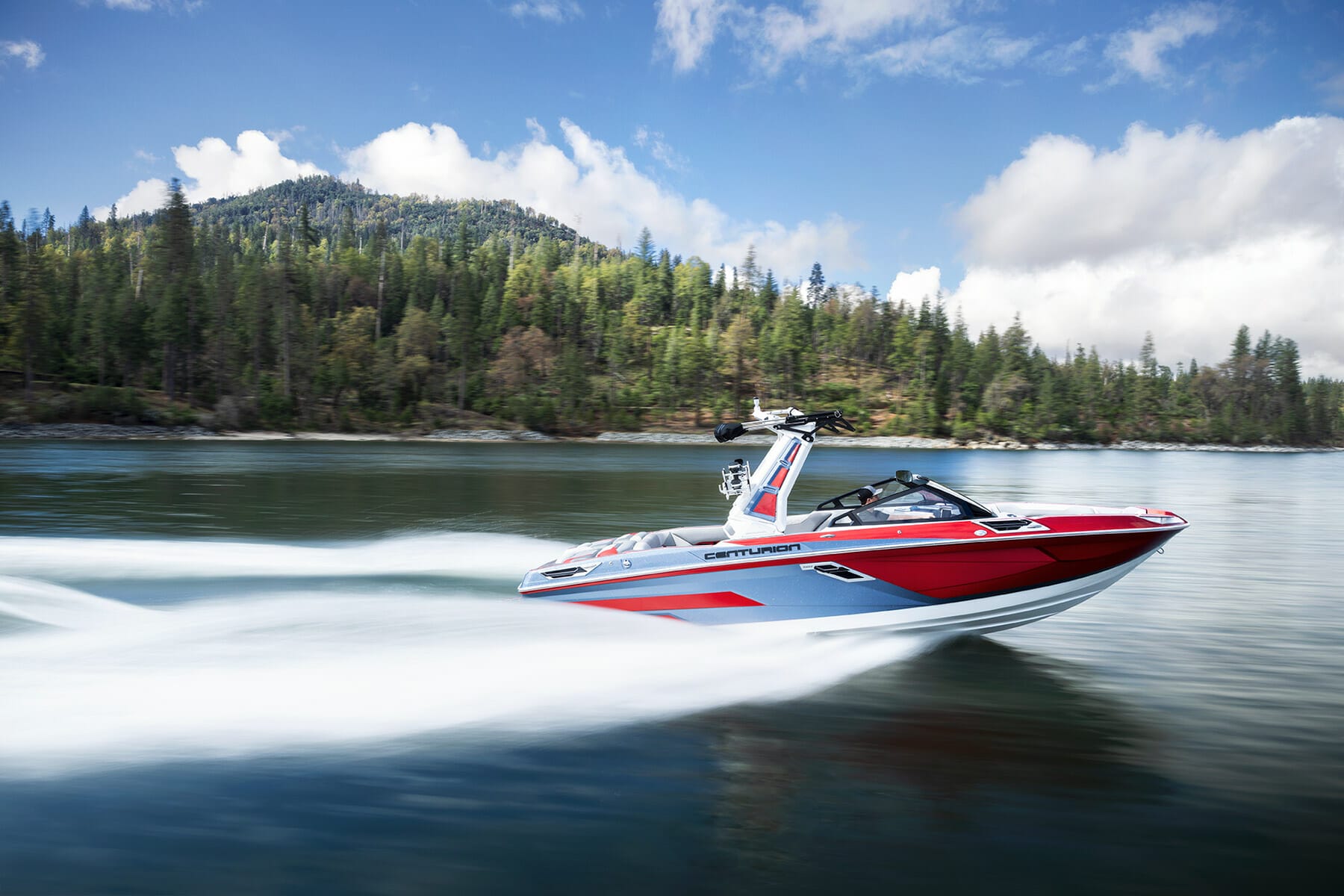 A red and white wakeboat speeding through a body of water.
