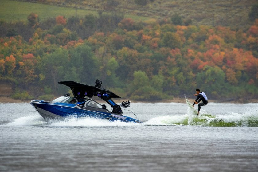A man is riding a wakesurf boat on the water.