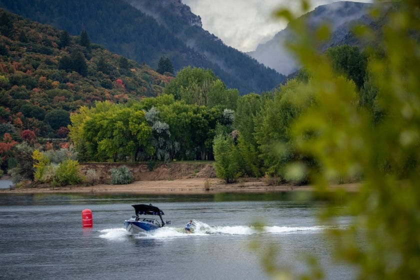 A wakesurf boat on a lake with mountains in the background.