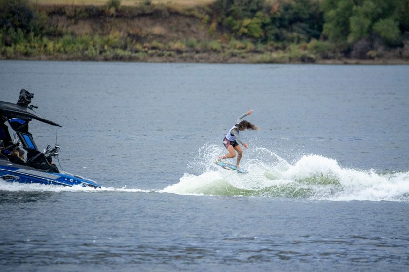 A woman is riding a wave on a wakesurf board near a boat.