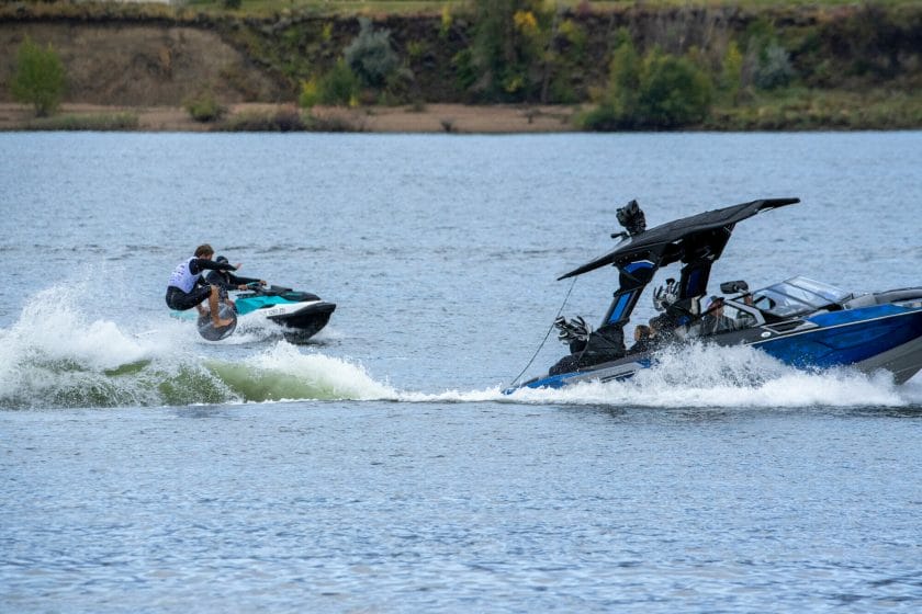 Two people riding a jet ski on a lake, wakesurf board.