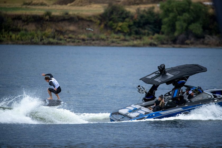 A man is riding a wakeboard behind a boat in wakesurfing style.
