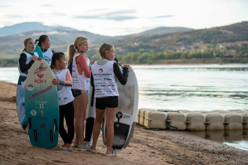 A group of girls standing on a beach with surfboards ready for wakesurfing.