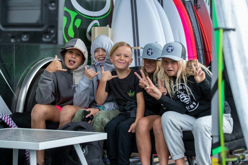 A group of kids are posing for a photo with their wakesurf boards.