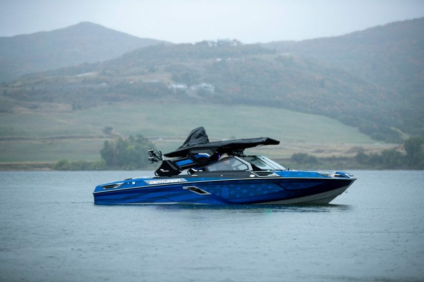 A wakesurf boat on a lake with mountains in the background.