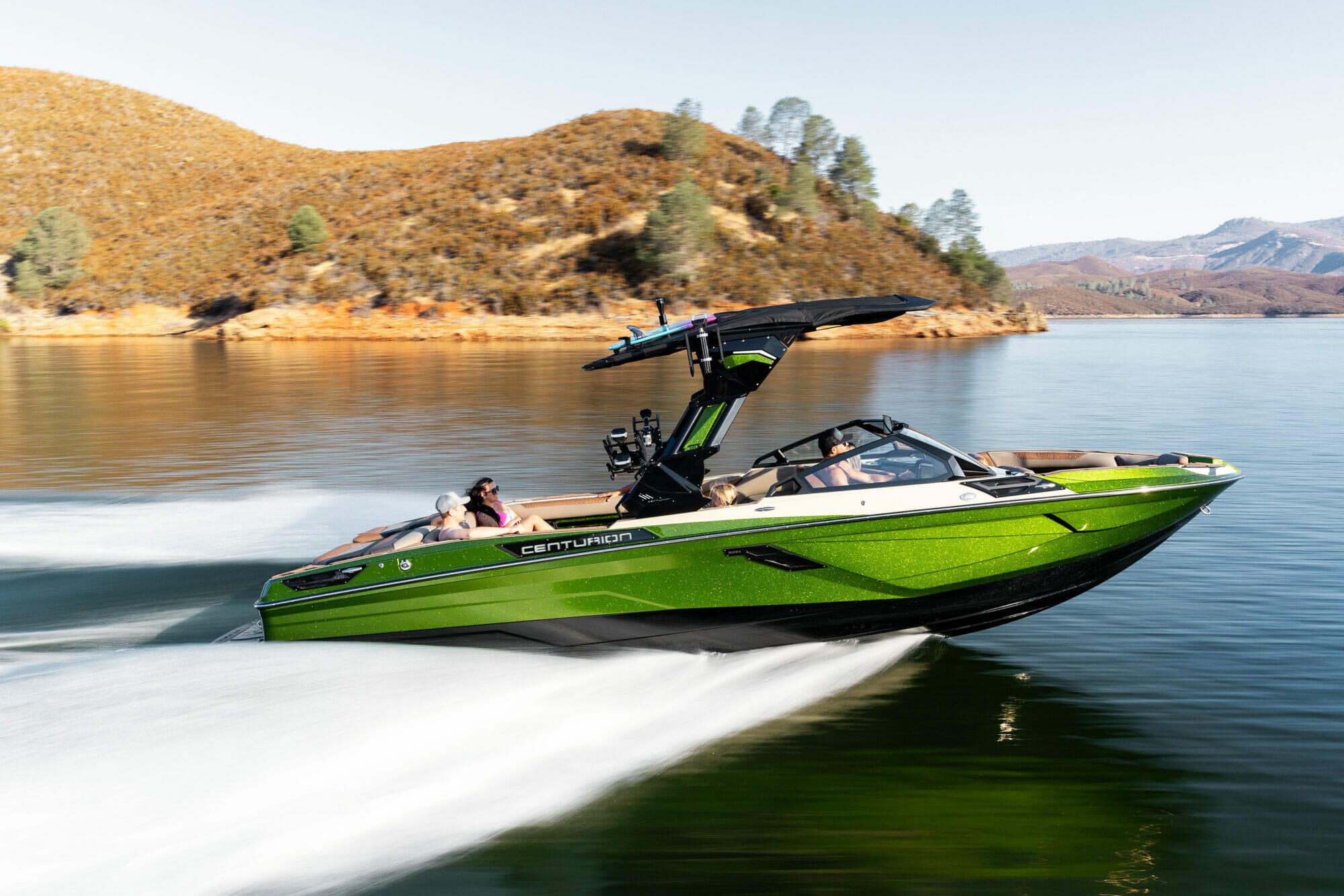 A green wakeboat is speeding through a body of water.