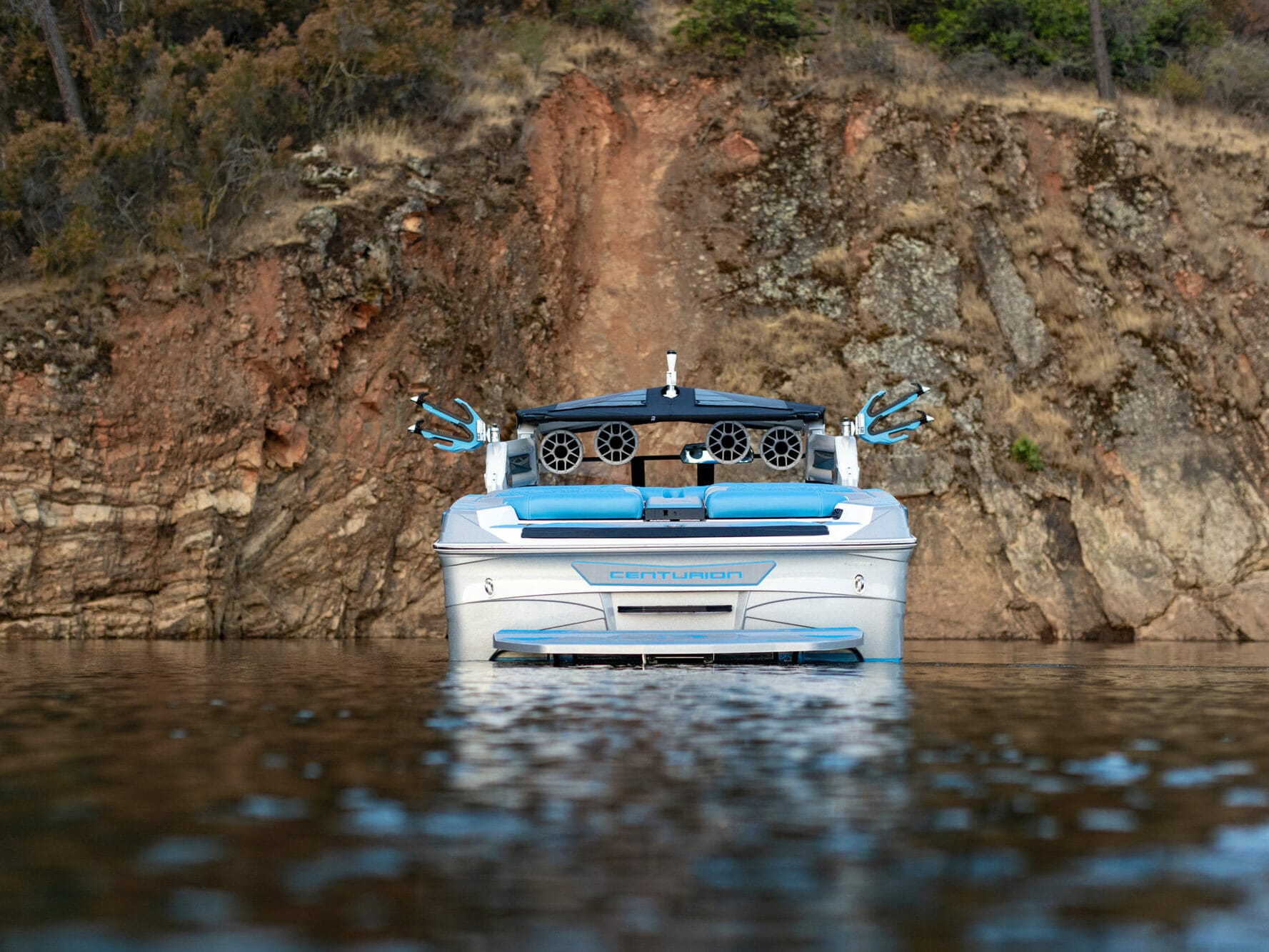 A wakesurf board is floating in the water near a cliff.