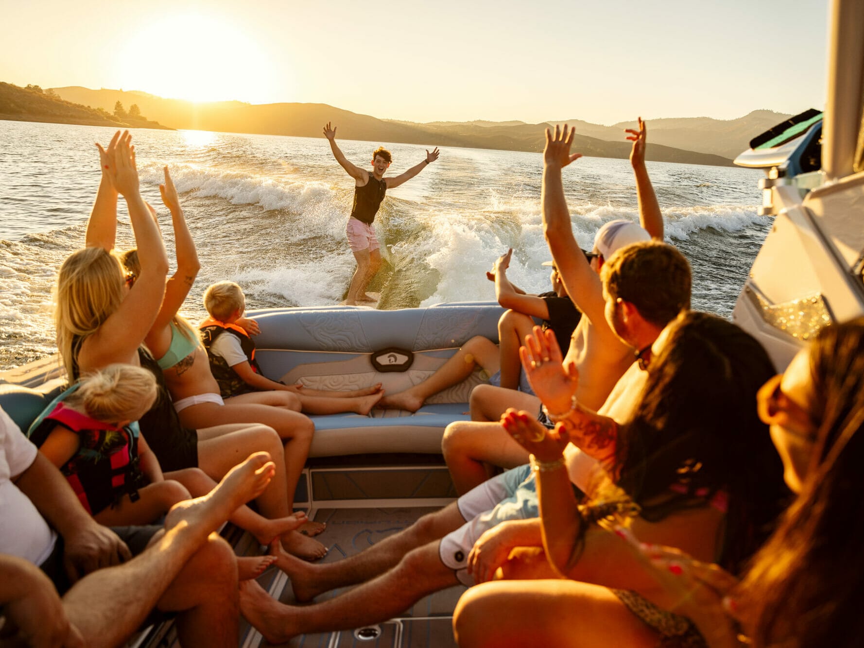 A group of people on a wakeboat with their arms up.