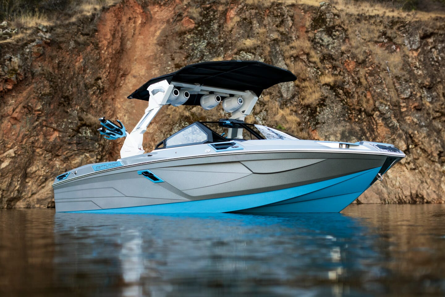 A blue wakeboat on the water near a cliff.