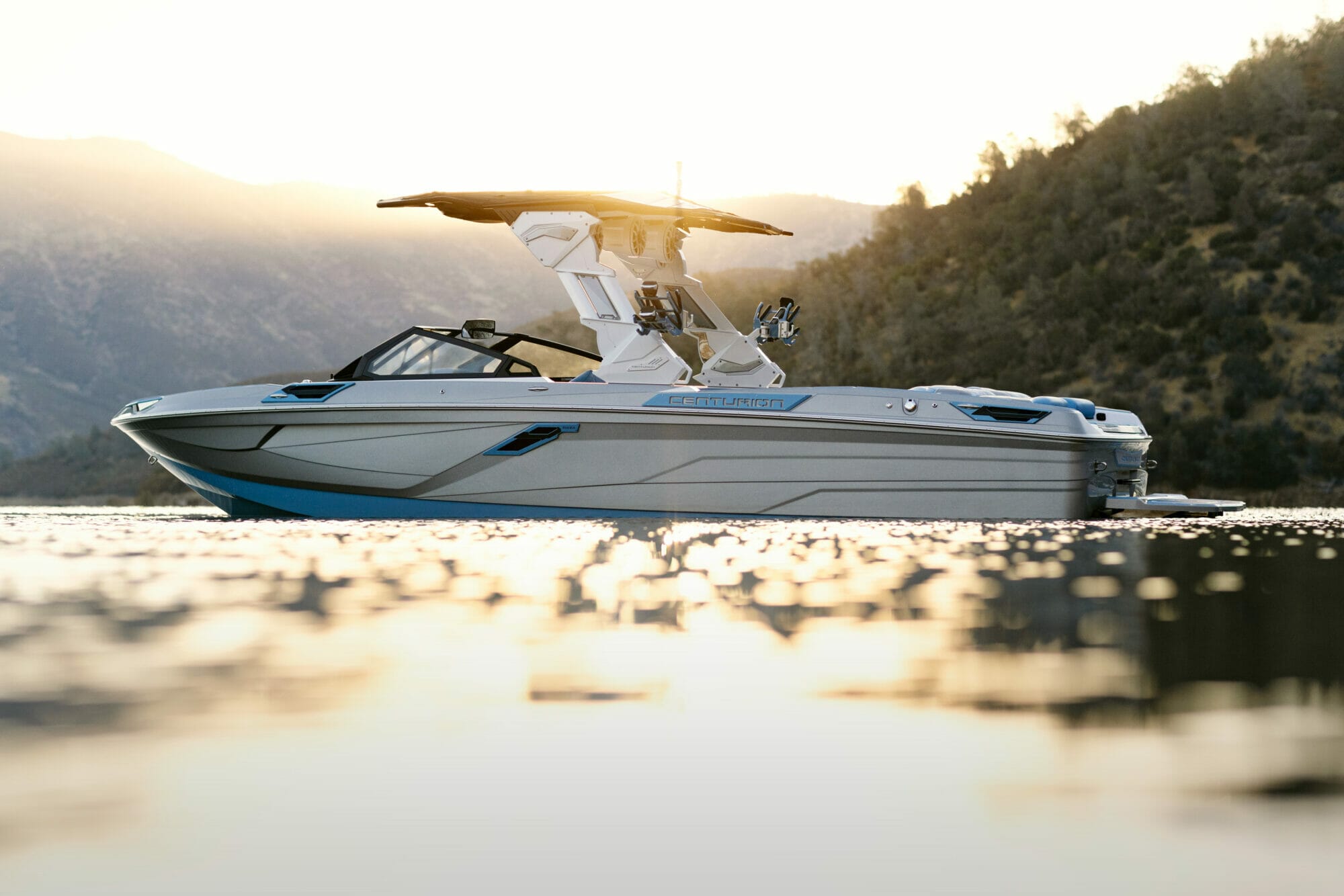 A wakeboat on the water with mountains in the background.