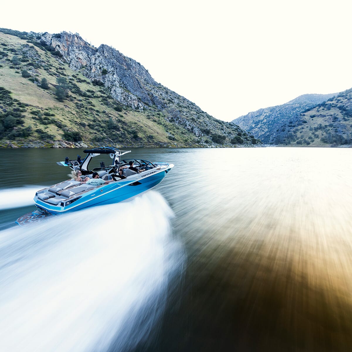 A Centurion Fe22 speedboat moves swiftly across a narrow river flanked by steep, green hills under a clear sky.
