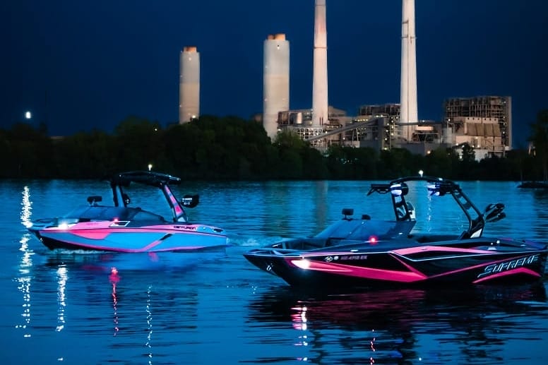 Two pink boats in the water at night near a power plant.