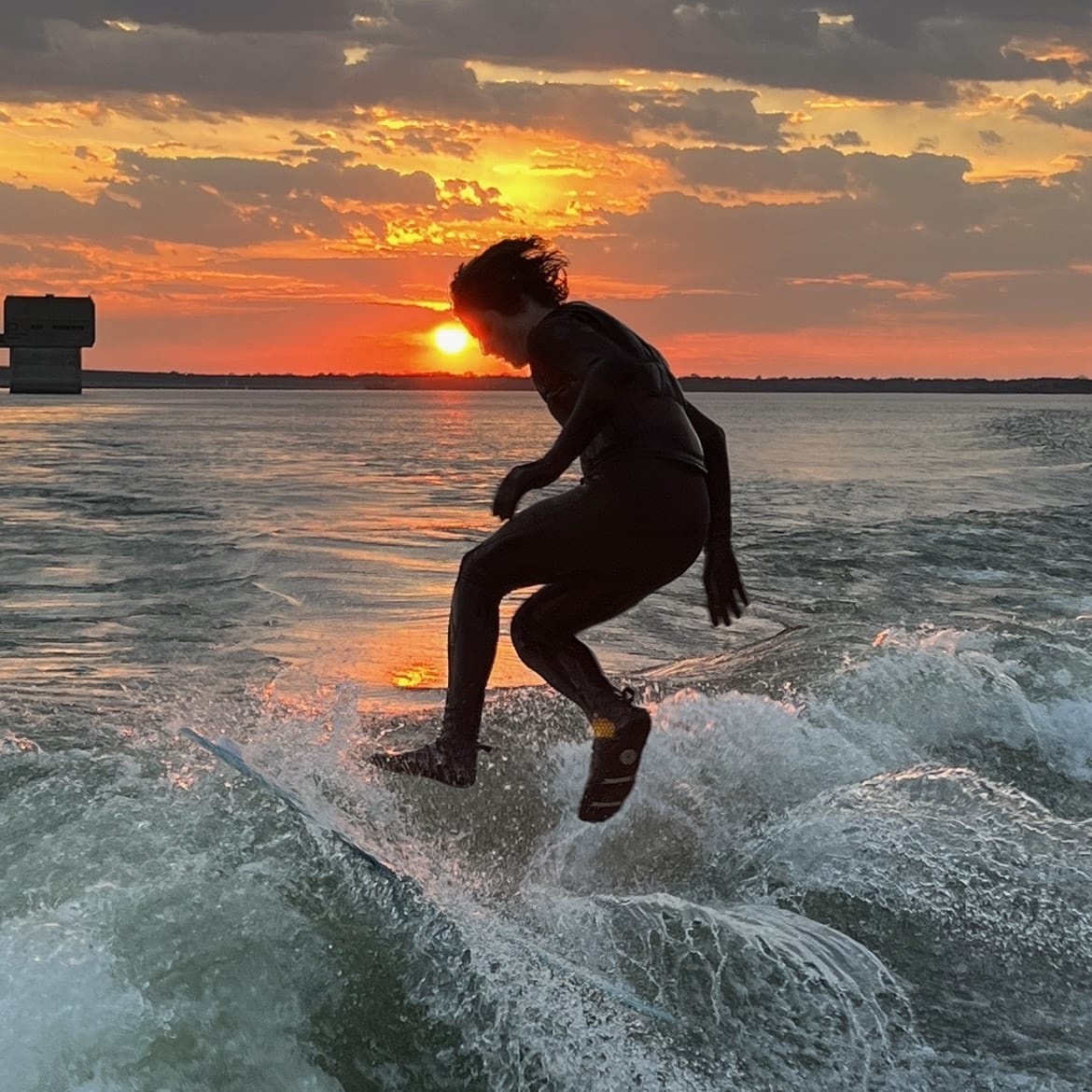 A person in a wetsuit riding a surfboard at sunset.